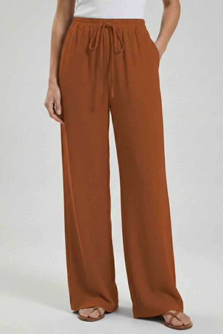 Women’s palazzo trousers with drawstring waist and side pockets by Jesie-London, featuring flowy fabric and relaxed fit.