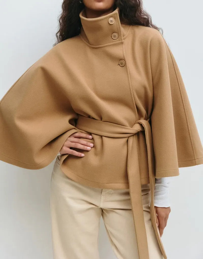 Women’s spring belted high-neck cape coat by Jesie-London featuring a funnel neck, waist belt, and cape sleeves.